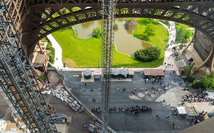 Eiffel Tower view from elevator, showing base structure and surrounding park in Paris.