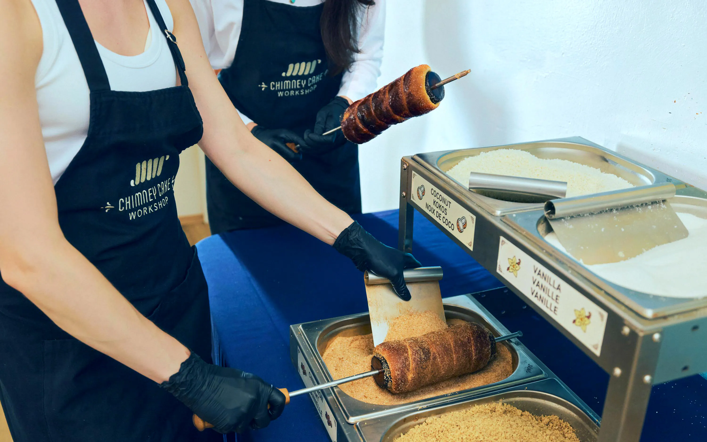 Participants preparing chimney cakes at a workshop in Budapest, rolling dough in sugar and coconut.