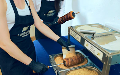 Participants preparing chimney cakes at a workshop in Budapest, rolling dough in sugar and coconut.
