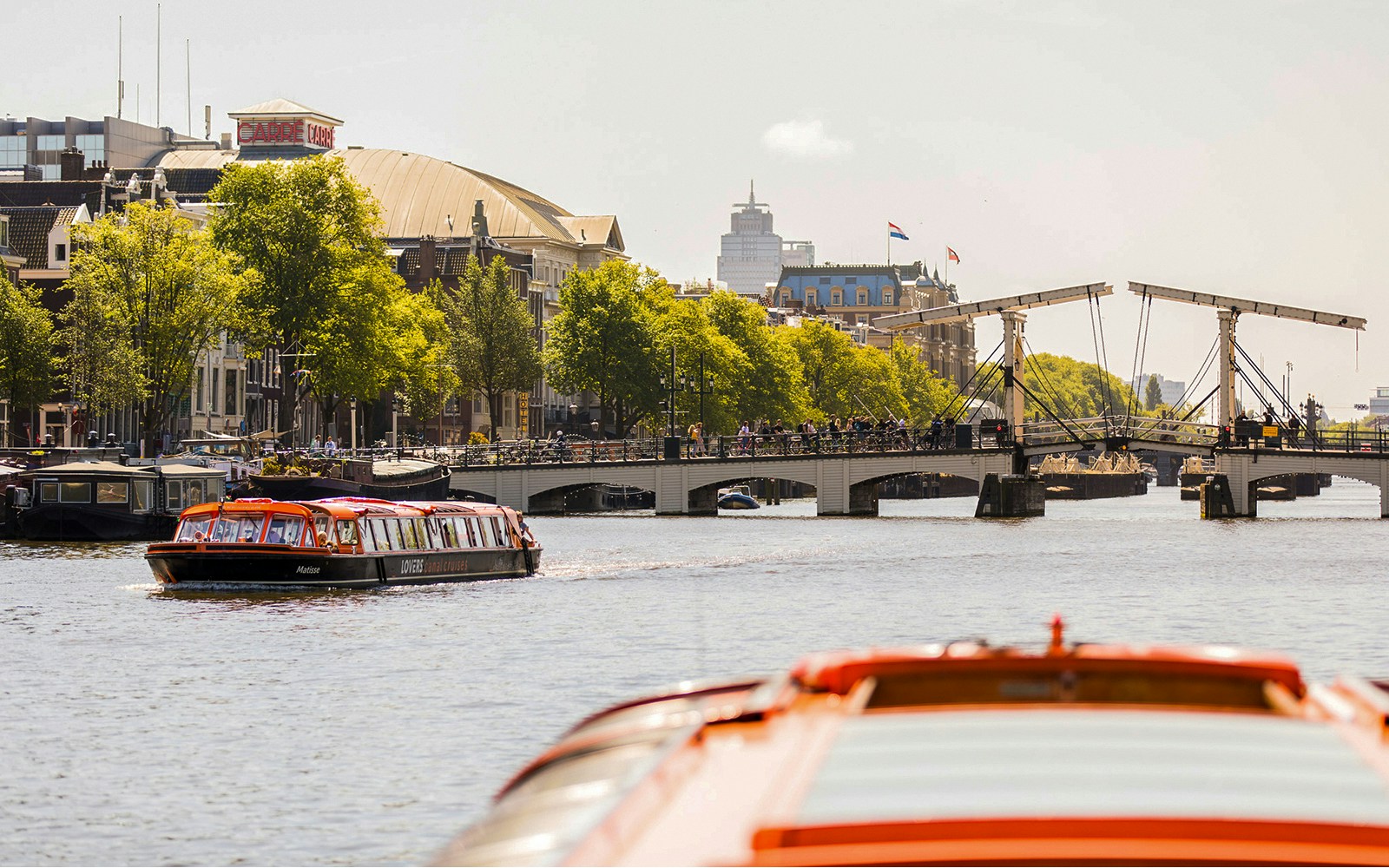Amsterdam canal cruise boat near Magere Brug with cityscape in background.