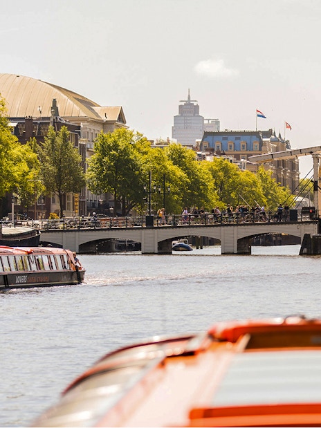 Amsterdam canal cruise boat near Magere Brug with cityscape in background.
