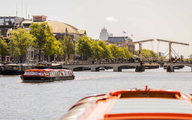 Amsterdam canal cruise boat near Magere Brug with cityscape in background.