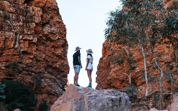 Couple standing on rock between red cliffs in Uluru-Kata Tjuta National Park.