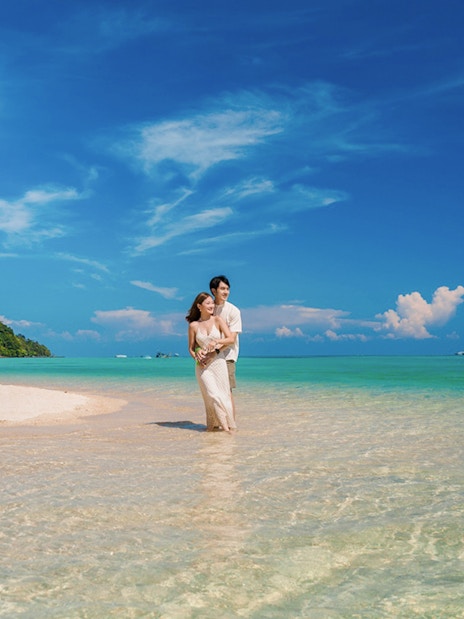 Tourists standing in clear water at Chong Khad Bay with lush green hills in the background.