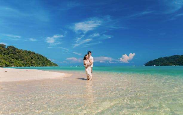 Tourists standing in clear water at Chong Khad Bay with lush green hills in the background.