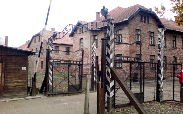 Entrance gate of Auschwitz-Birkenau concentration camp with brick buildings in the background.