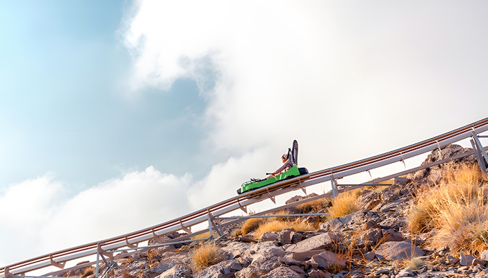 Solo rider on the Jais Sledder, navigating down a mountain track against a backdrop of rocky terrain and blue sky in Ras Al Khaimah, UAE