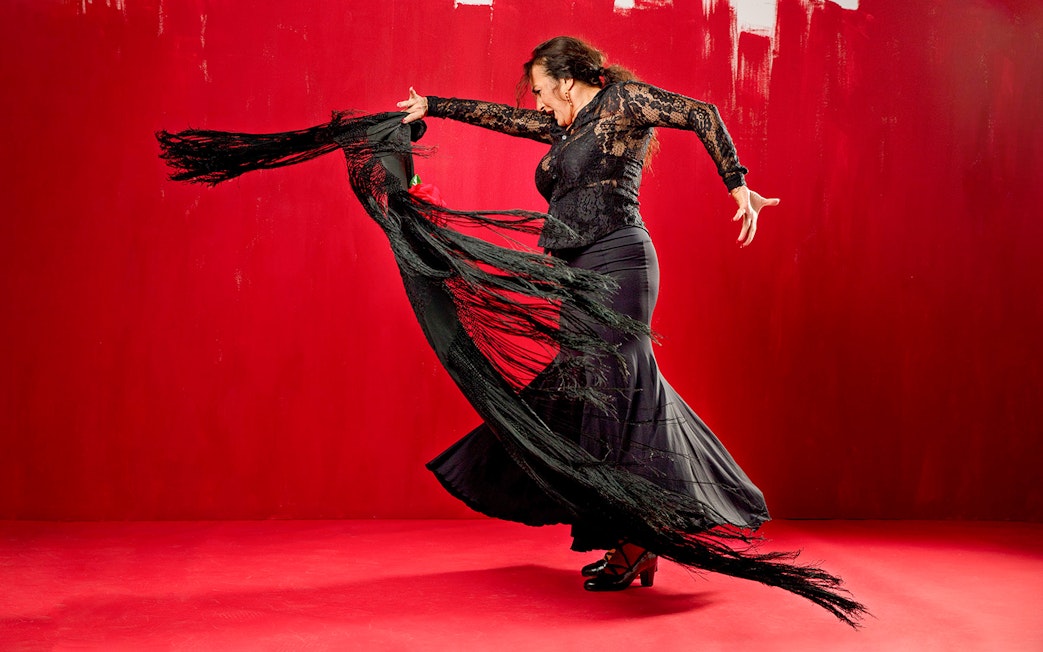 Flamenco dancer performing with a black shawl against a red background at Esencia espectáculo.