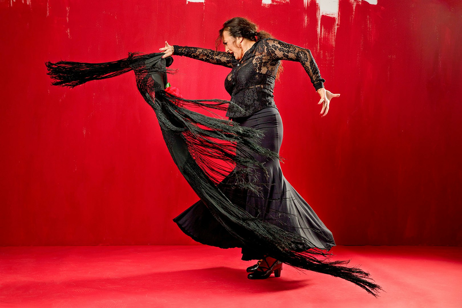 Flamenco dancer performing with a black shawl against a red background at Esencia espectáculo.