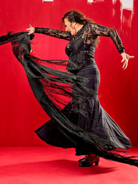 Flamenco dancer performing with a black shawl against a red background at Esencia espectáculo.