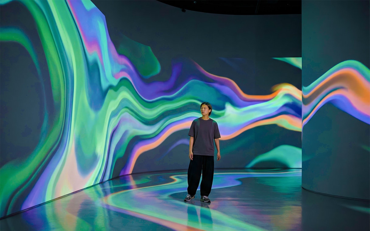 Guest surrounded by colorful light projections at an immersive art exhibit.