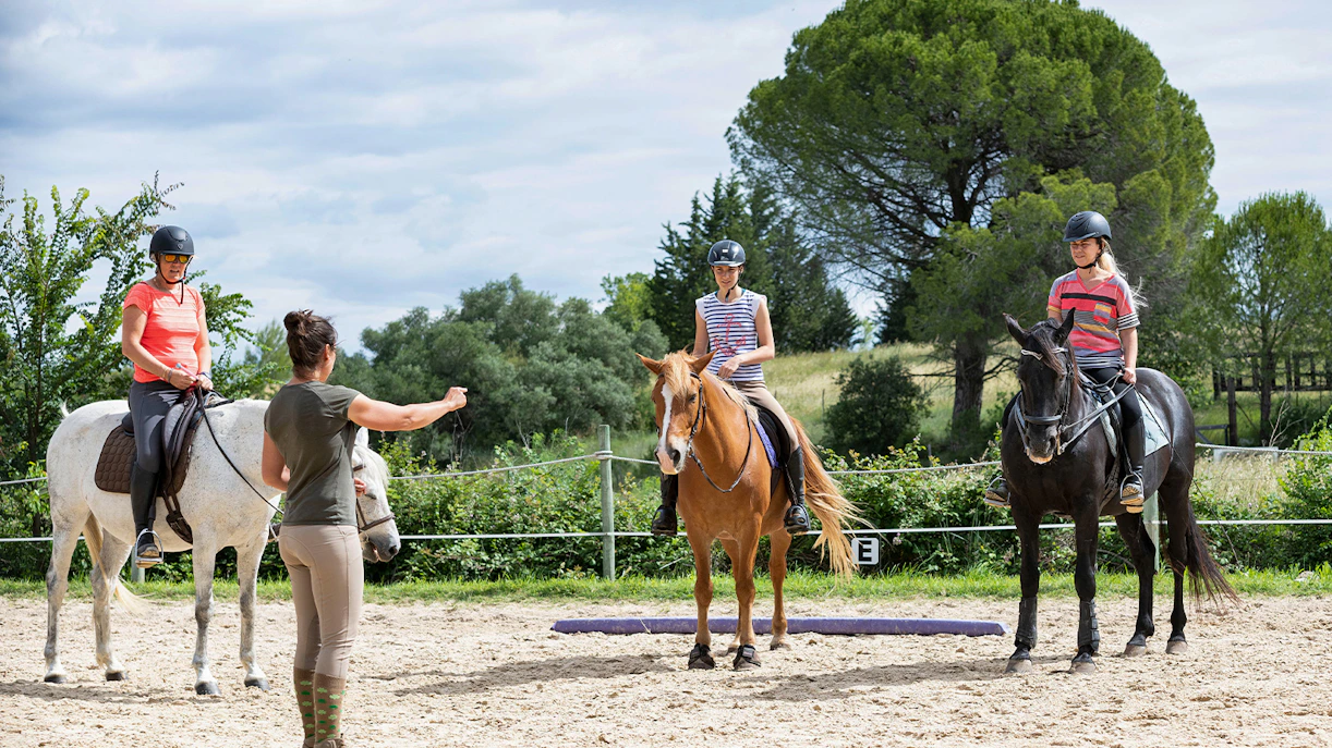Horse riding lesson with instructor guiding three riders in an outdoor arena.