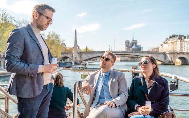 People enjoying champagne on a Seine River cruise with Notre-Dame in the background.