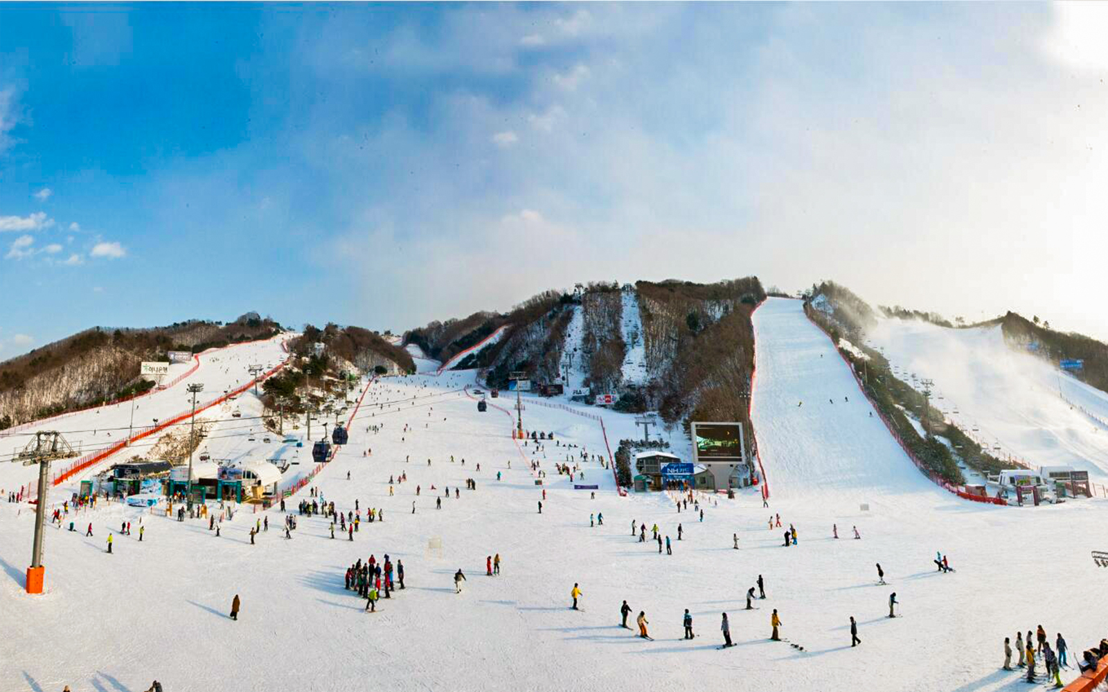 Skiers and snowboarders at Vivaldi Park Snowy Land, South Korea, with snowy slopes and ski lifts.
