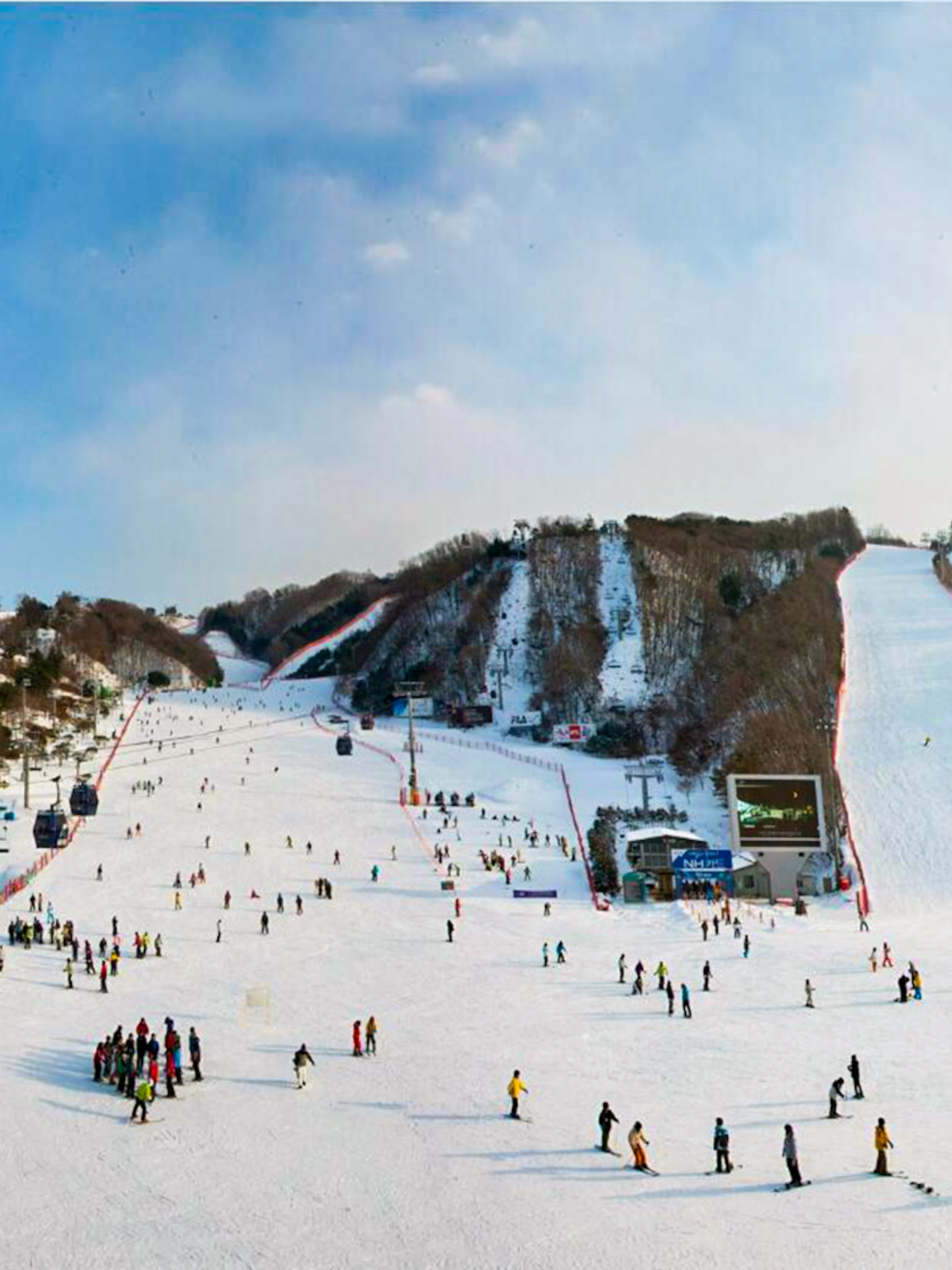 Skiers and snowboarders at Vivaldi Park Snowy Land, South Korea, with snowy slopes and ski lifts.