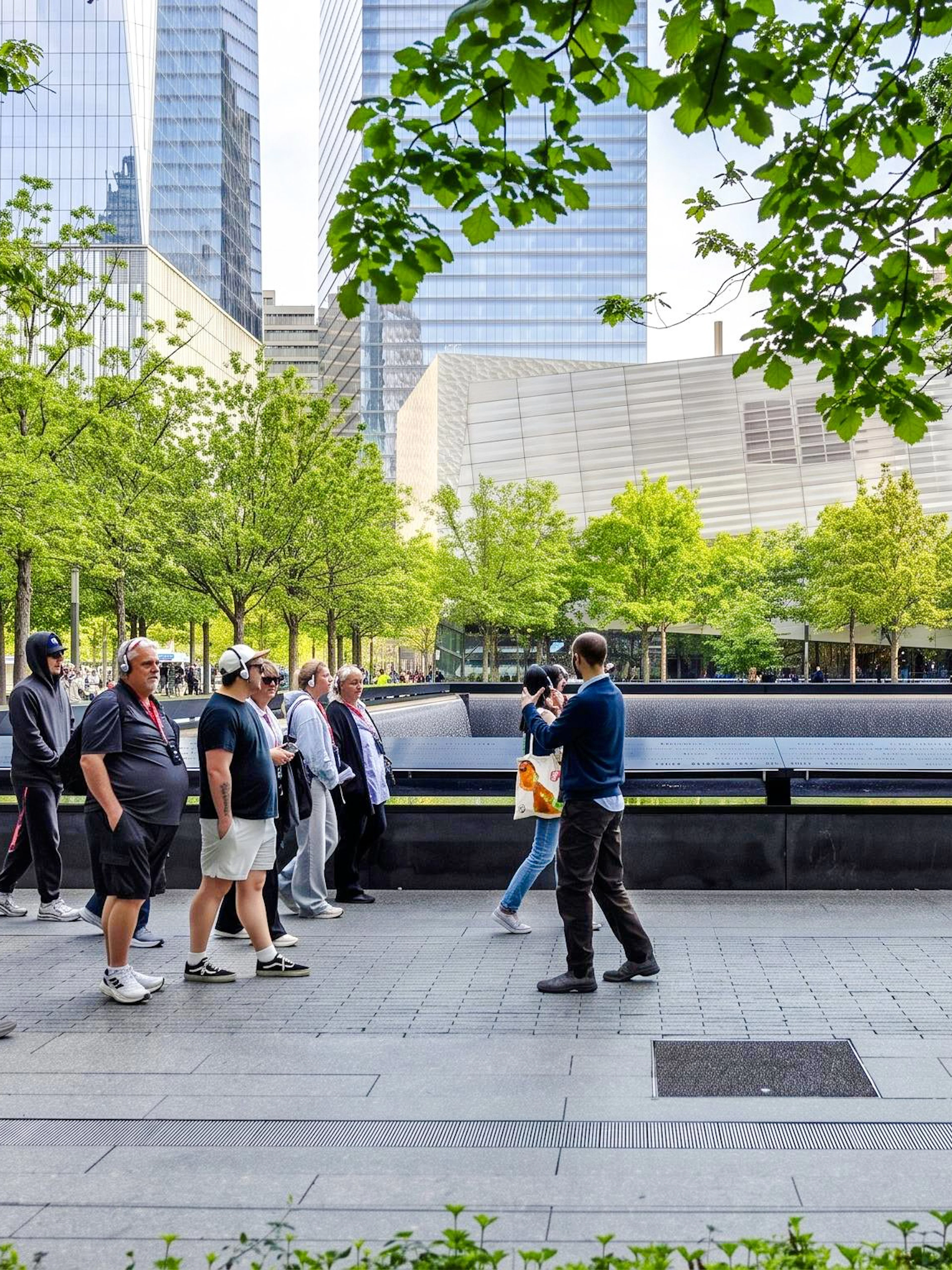 #Visitors at the 9/11 Memorial in New York City, with trees and skyscrapers in the background.
