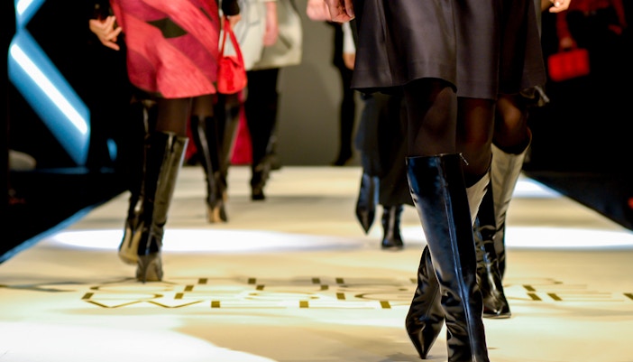 Models walking on a runway during fashion week, showcasing designer boots and dresses.