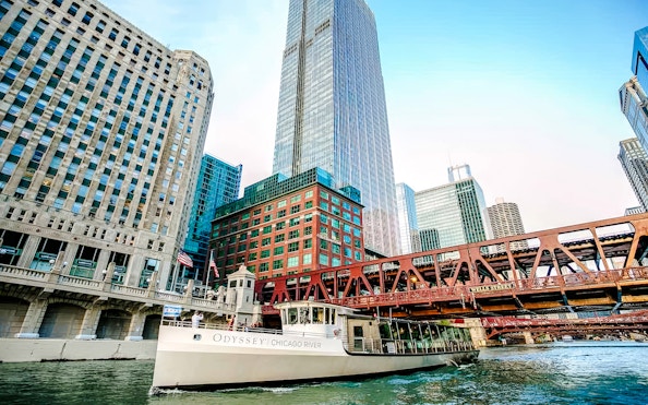 Cruise boat on Chicago River with city skyscrapers and bridge in view.