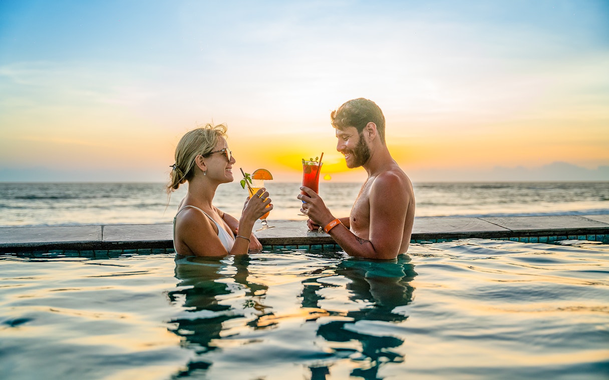 People enjoying drinks in the pool at Atlas Beach Club, Bali during sunset.