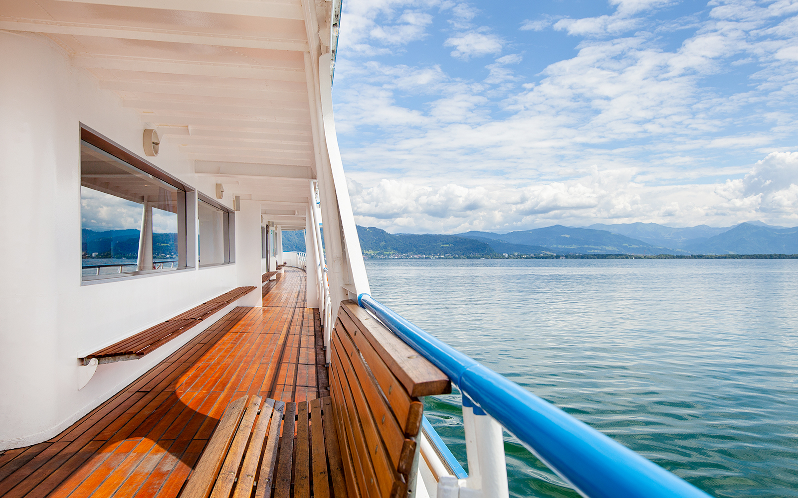 Ferry deck overlooking a calm lake with distant mountains.
