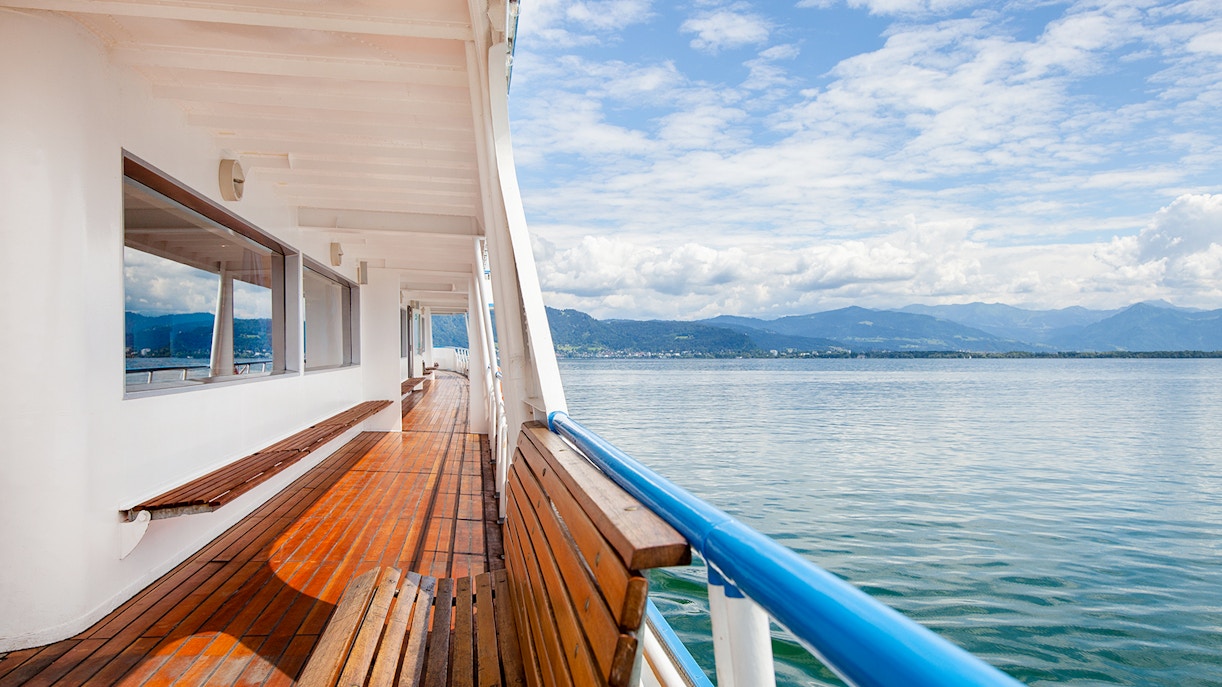Ferry deck overlooking a calm lake with distant mountains.
