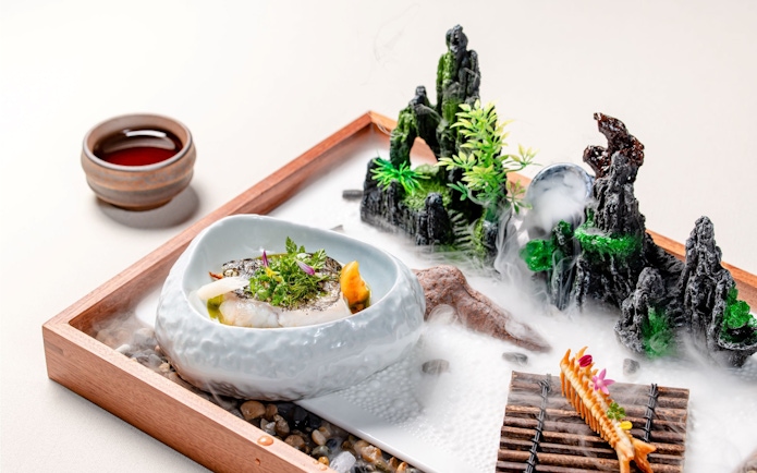 Curated dish on themed tray with miniature landscape at Taste of China, Shanghai.
