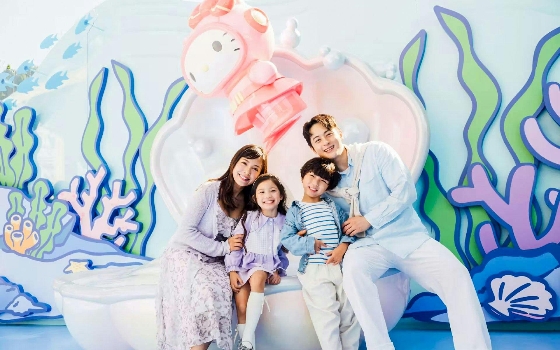 Family smiling in front of a colorful marine-themed backdrop at Ocean Park.