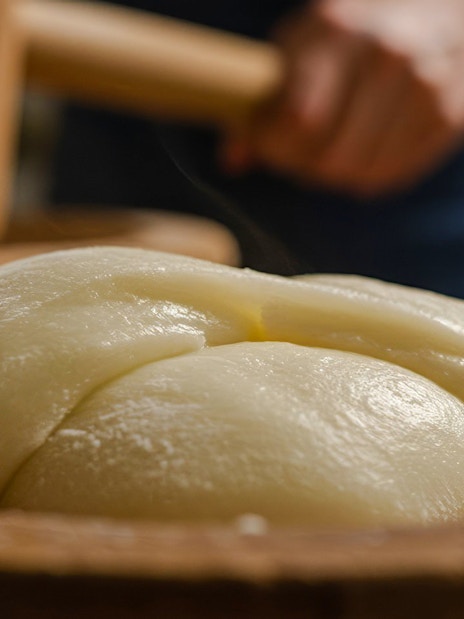 Man pounding mochi dough with a wooden mallet in a traditional setting.