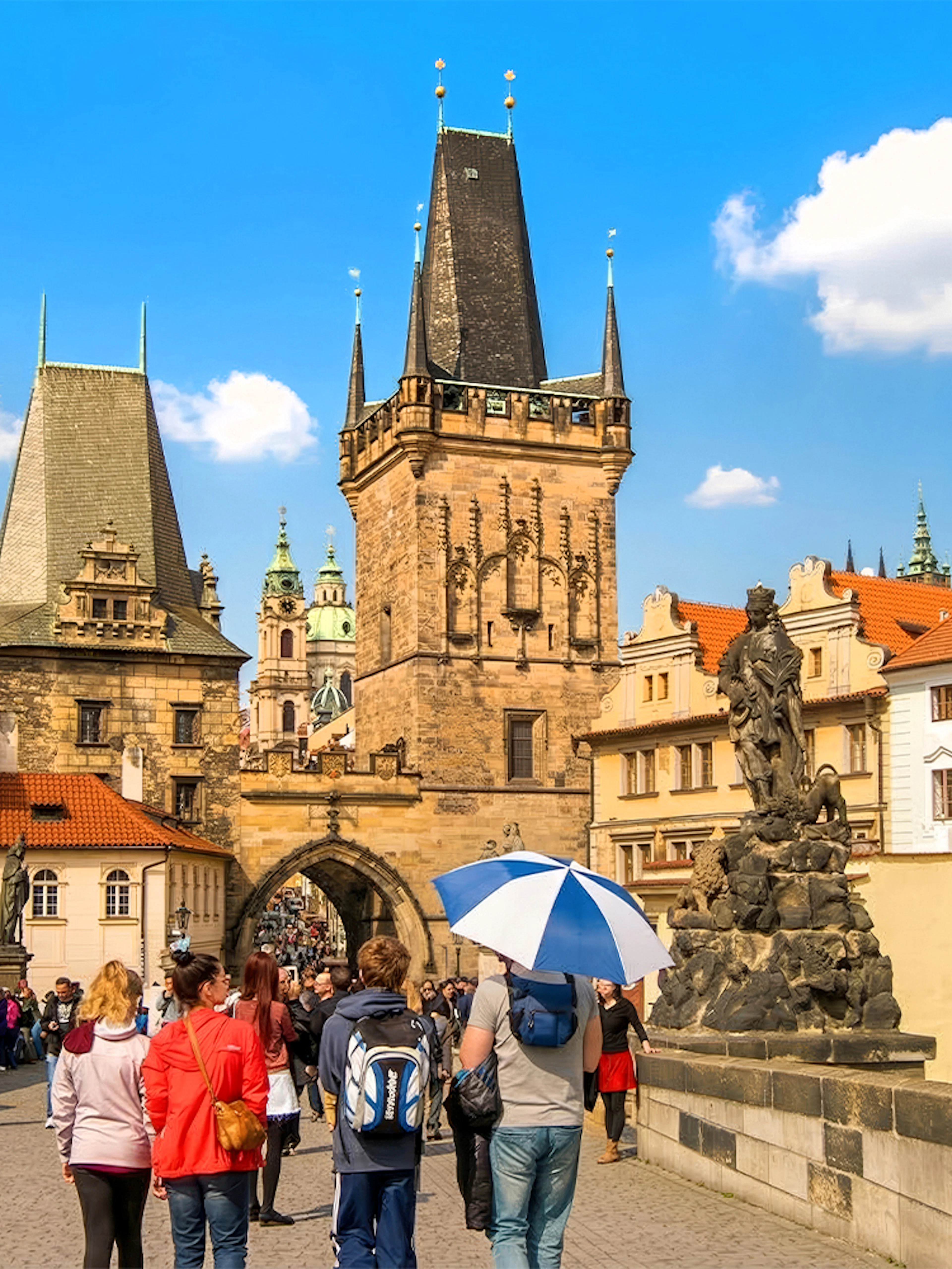 Guests walking on Charles Bridge, Prague, near Malá Strana with historic towers and statues.