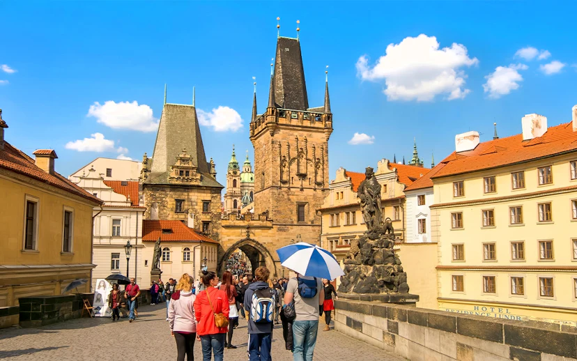 Guests walking on Charles Bridge, Prague, near Malá Strana with historic towers and statues.