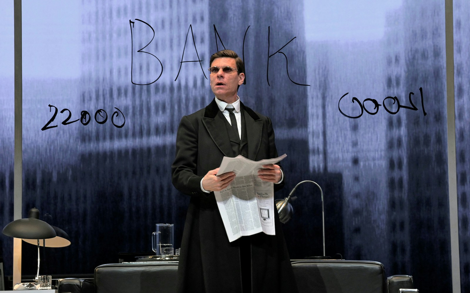 Actor on stage holding a newspaper in "The Lehman Trilogy" play.
