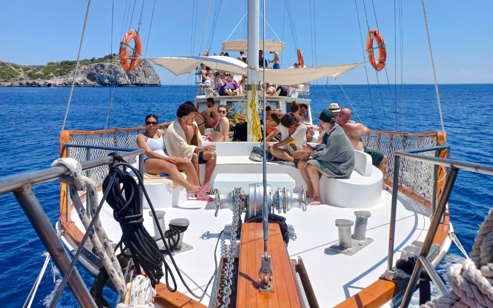 People relaxing on a daytime cruise from Rhodes, with a view of the sea and distant cliffs.