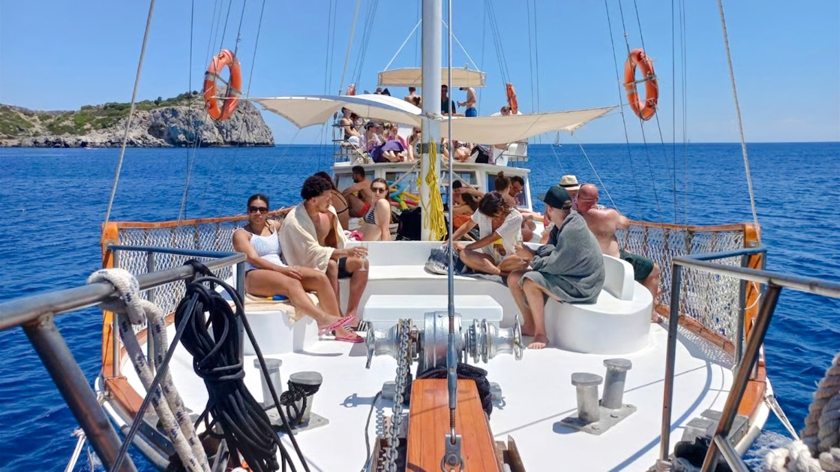 People relaxing on a daytime cruise from Rhodes, with a view of the sea and distant cliffs.