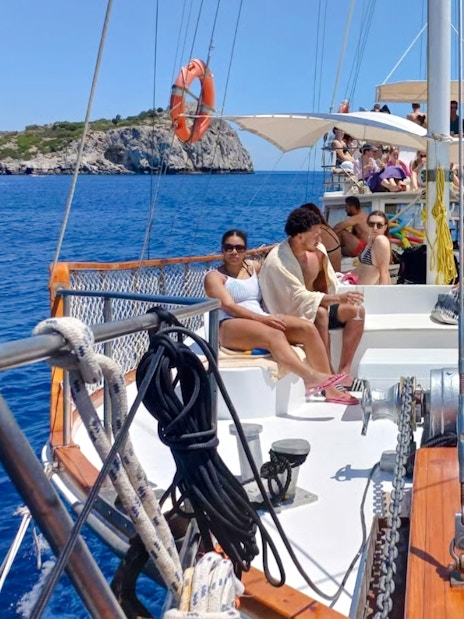 People relaxing on a daytime cruise from Rhodes, with a view of the sea and distant cliffs.