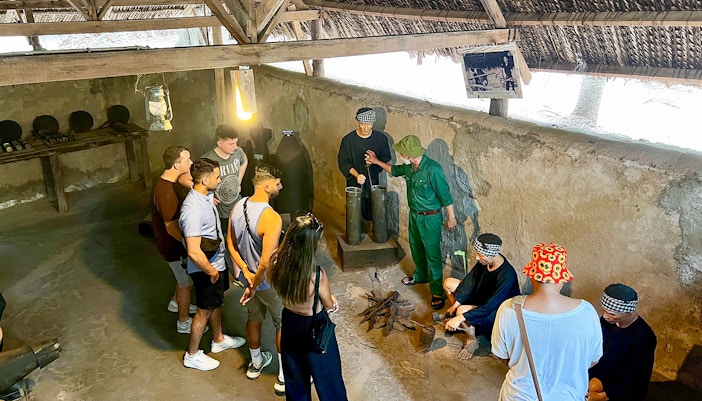 Tour group with guide exploring kitchen area in Cu Chi Tunnels, Ho Chi Minh City.