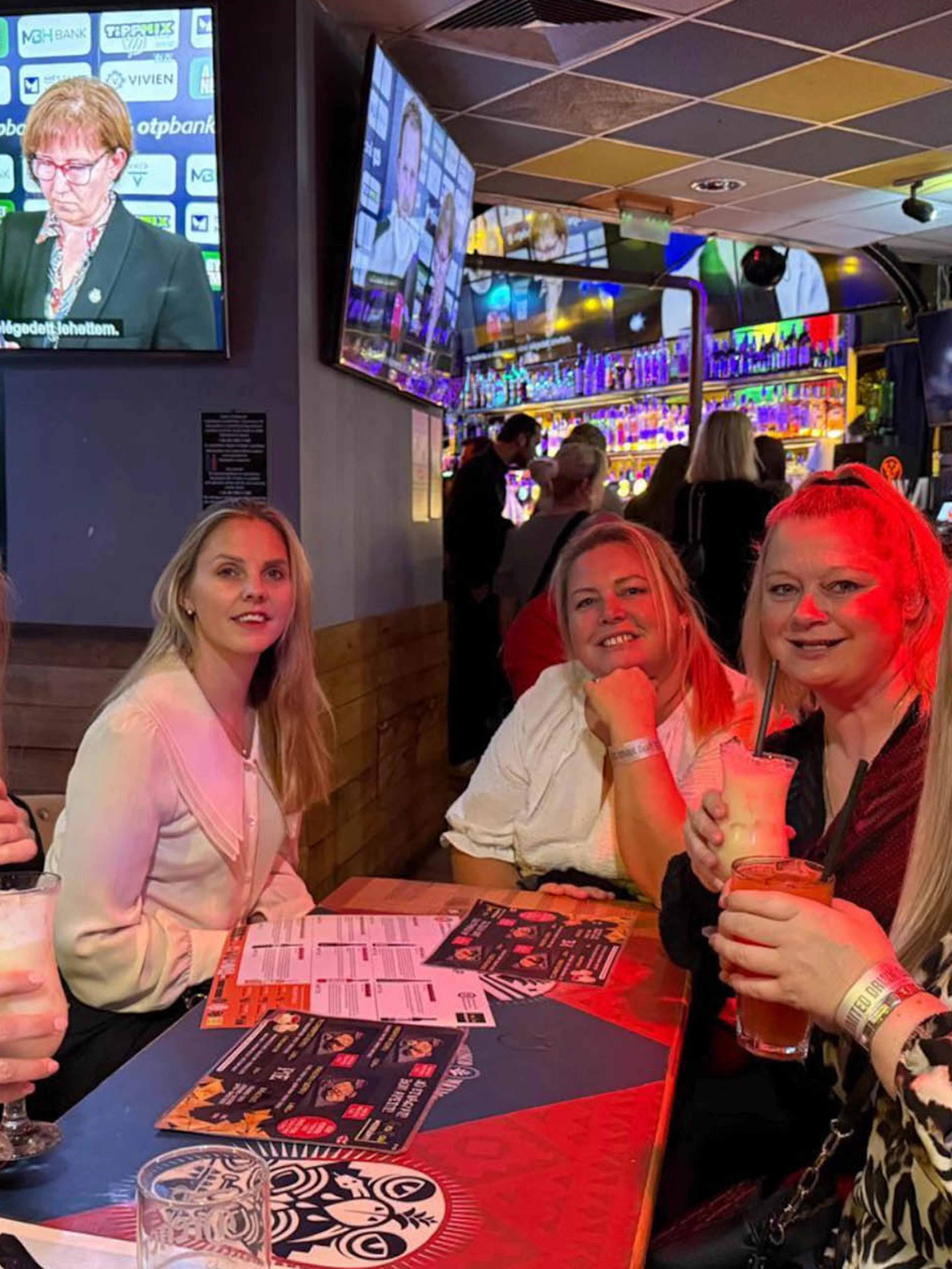 Group enjoying drinks at a lively pub during a bar tour, with sports on TV in the background.