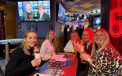 Group enjoying drinks at a lively pub during a bar tour, with sports on TV in the background.