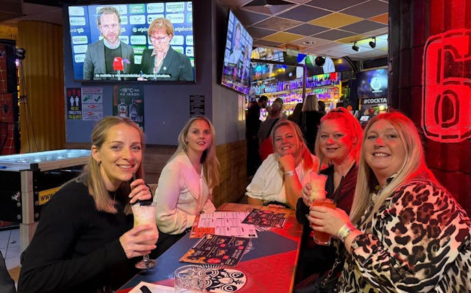 Group enjoying drinks at a lively pub during a bar tour, with sports on TV in the background.