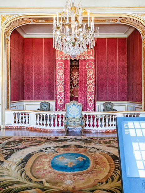 Chambord Castle interior with ornate red walls, chandelier, and decorative chairs.