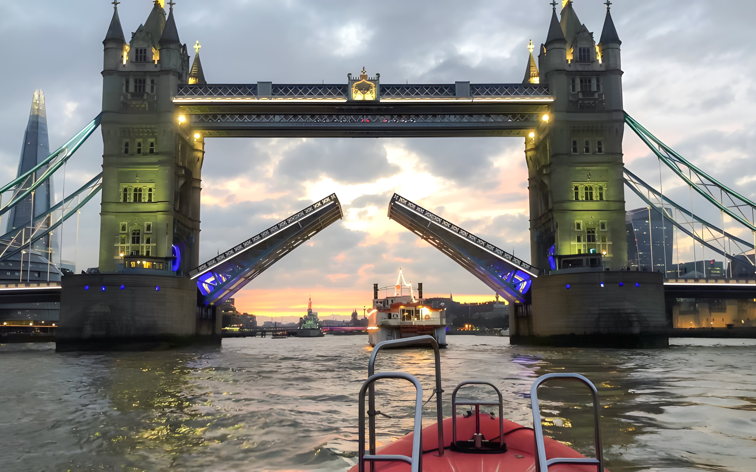 Tower Bridge opening for a speedboat on the Thames River during sunset in London.