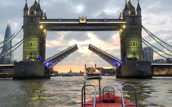 Tower Bridge opening for a speedboat on the Thames River during sunset in London.
