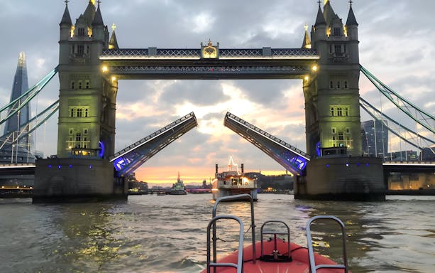Tower Bridge opening for a speedboat on the Thames River during sunset in London.