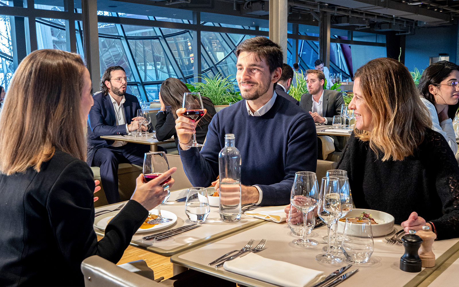 Mehrere Menschen sitzen mit einem Glas Wein in der Hand und Essen auf dem Tisch vor sich in einem Restaurant