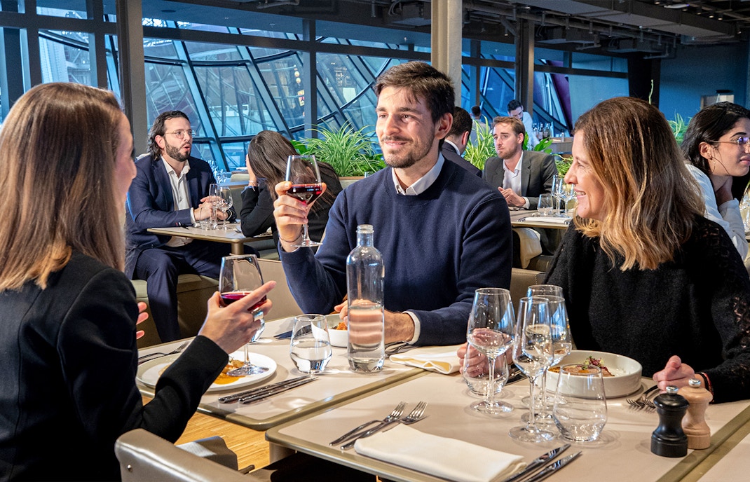 Mehrere Menschen sitzen mit einem Glas Wein in der Hand und Essen auf dem Tisch vor sich in einem Restaurant