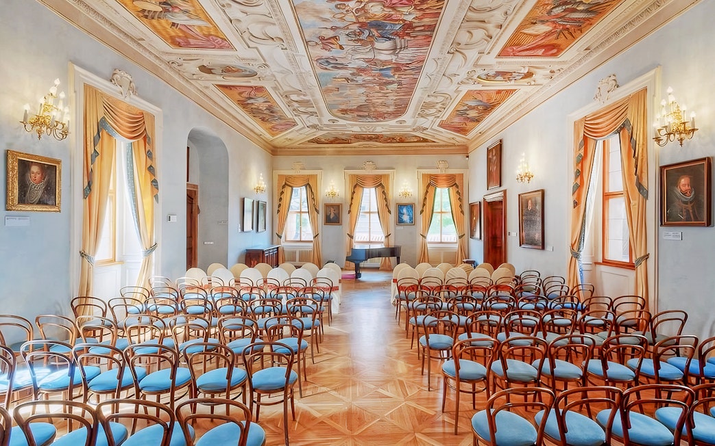 Interior of Lobkowicz Palace concert hall with ornate ceiling and rows of chairs.
