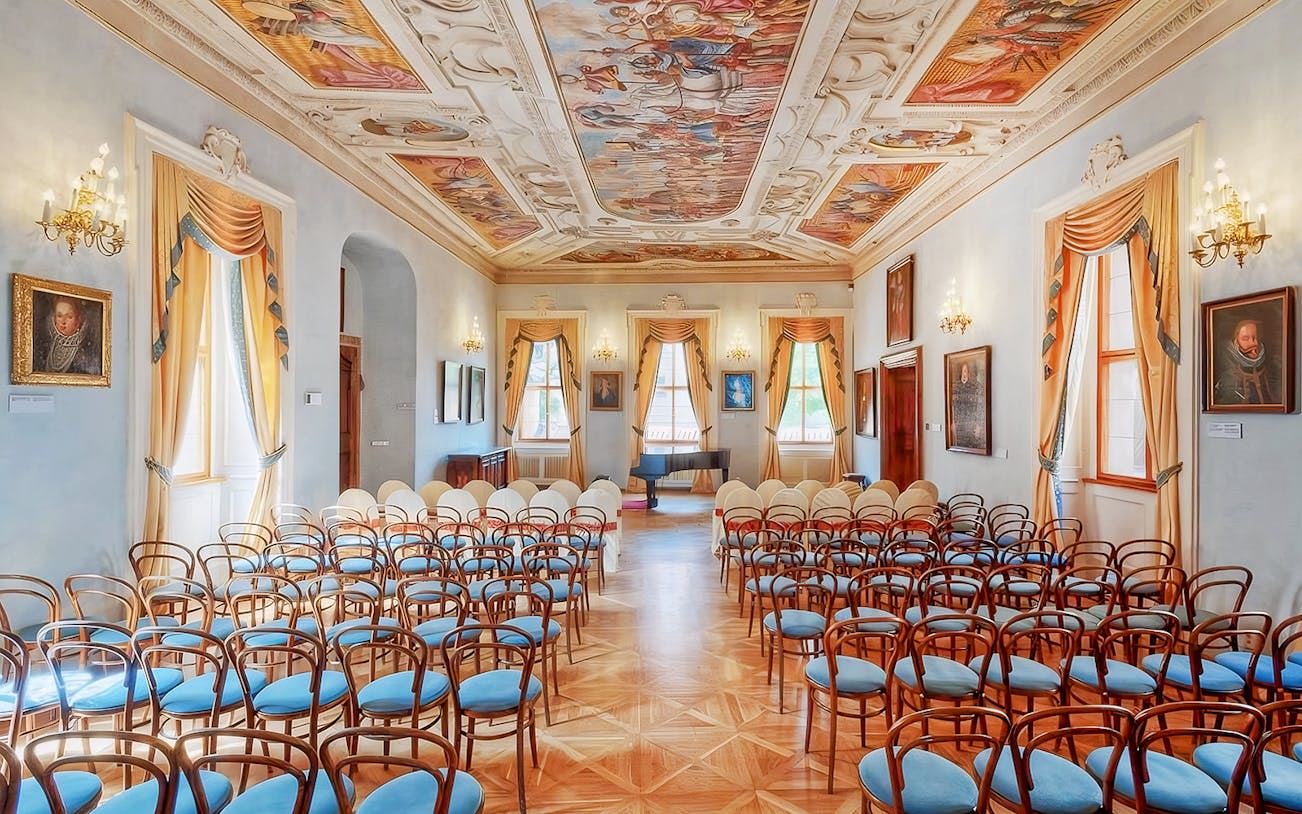 Interior of Lobkowicz Palace concert hall with ornate ceiling and rows of chairs.