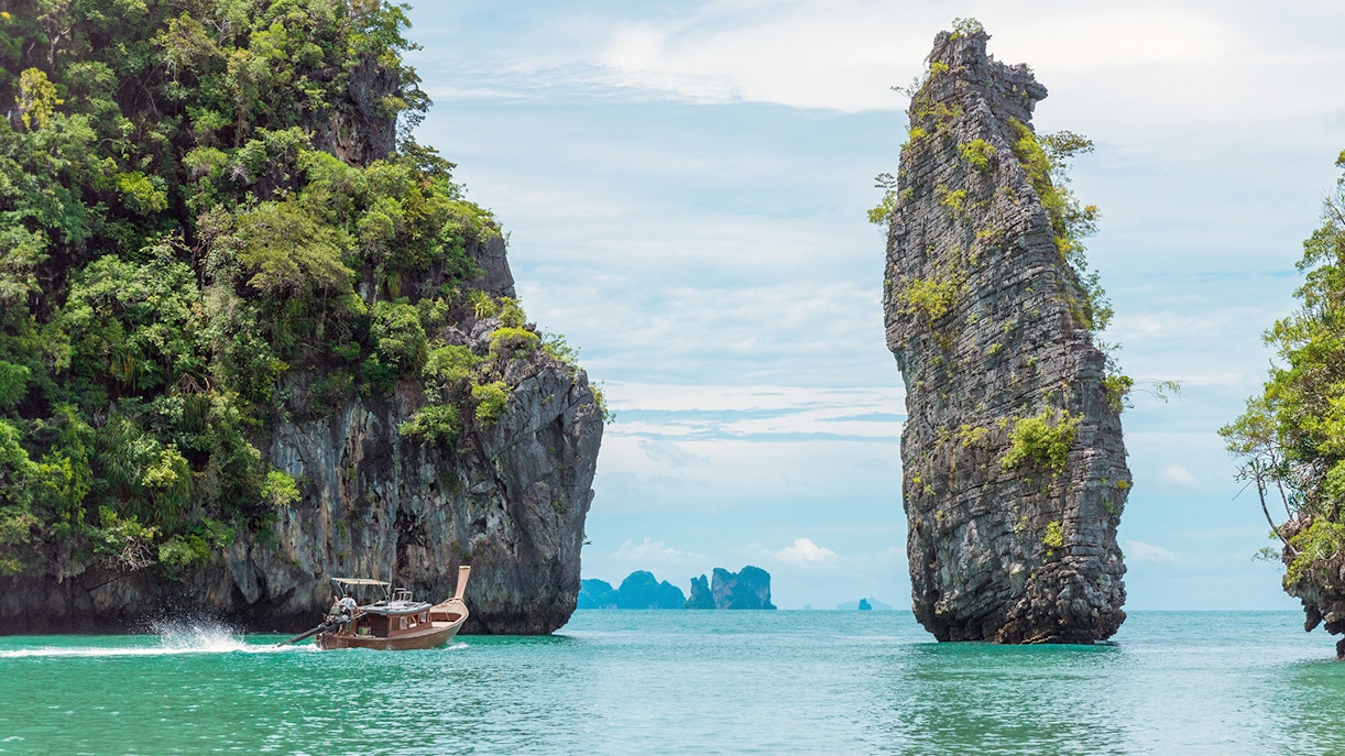 Longtail boat navigating between limestone cliffs in Phang Nga Bay, Thailand.
