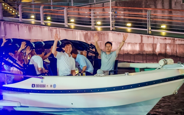Passengers waving on a boat during an Osaka Dotonbori River Cruise at night.