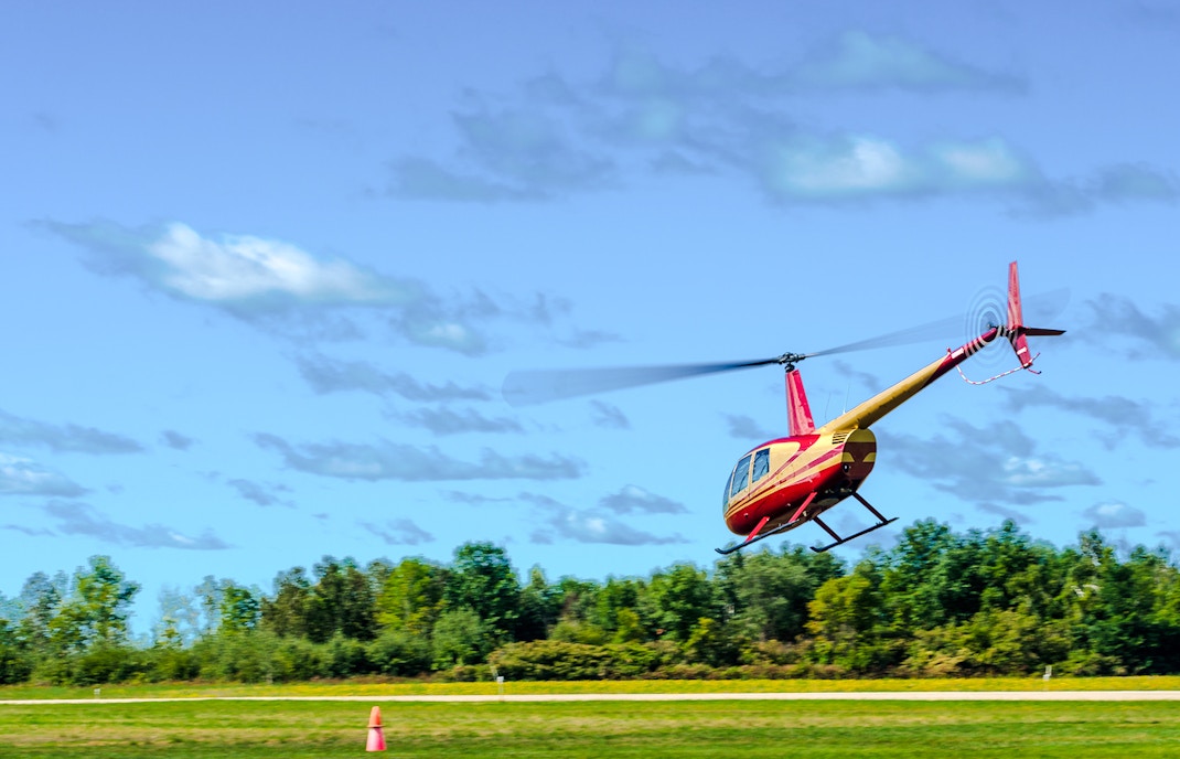 Helicopter taking off over grassy field with trees in the background.