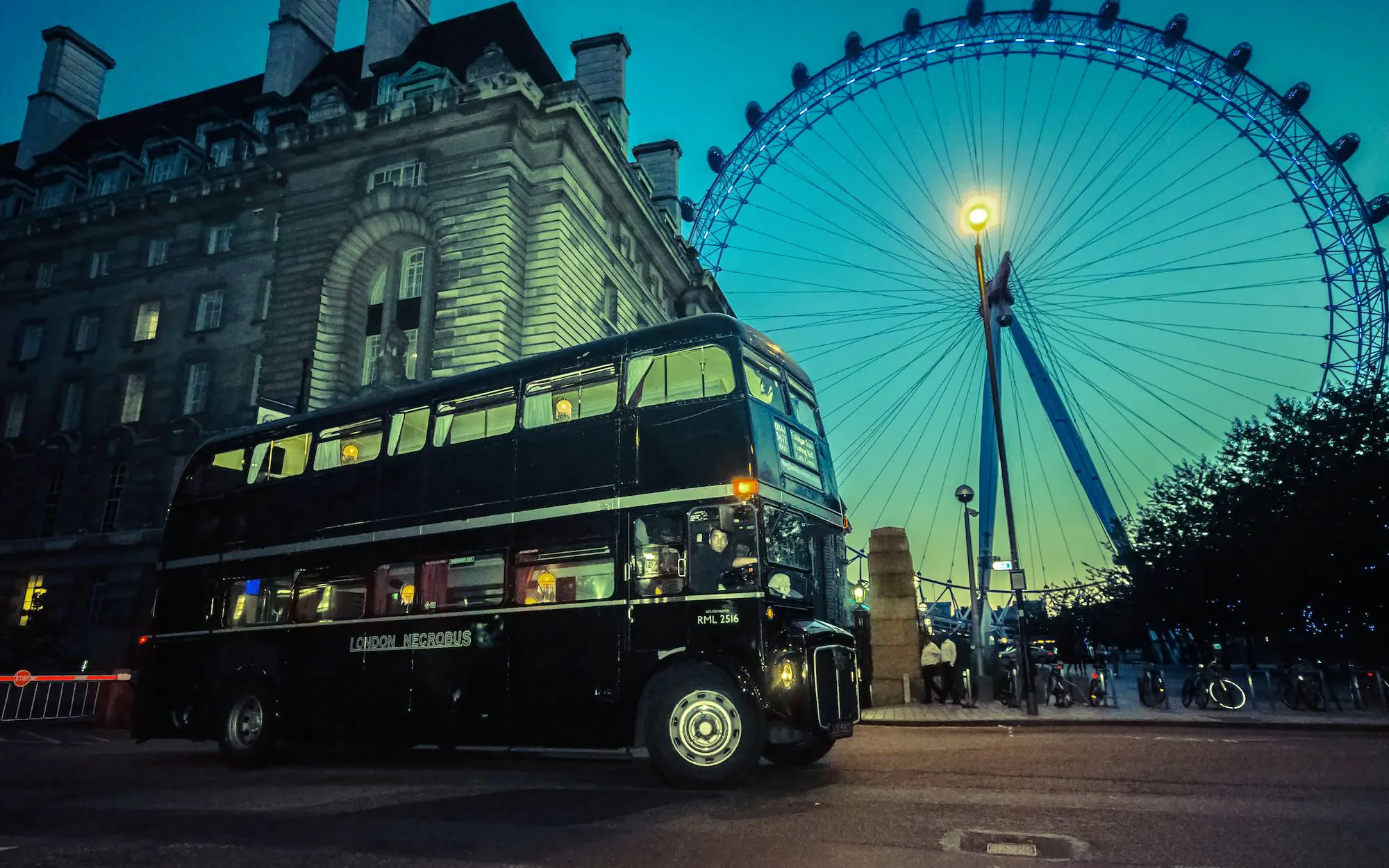 Vintage double-decker bus on London ghost tour near the London Eye at dusk.